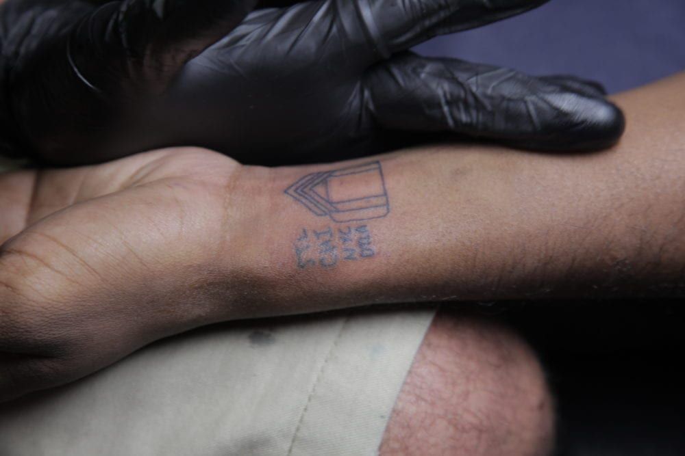 Wrist tattoo being worked on by gloved hand. Shows a book with words.