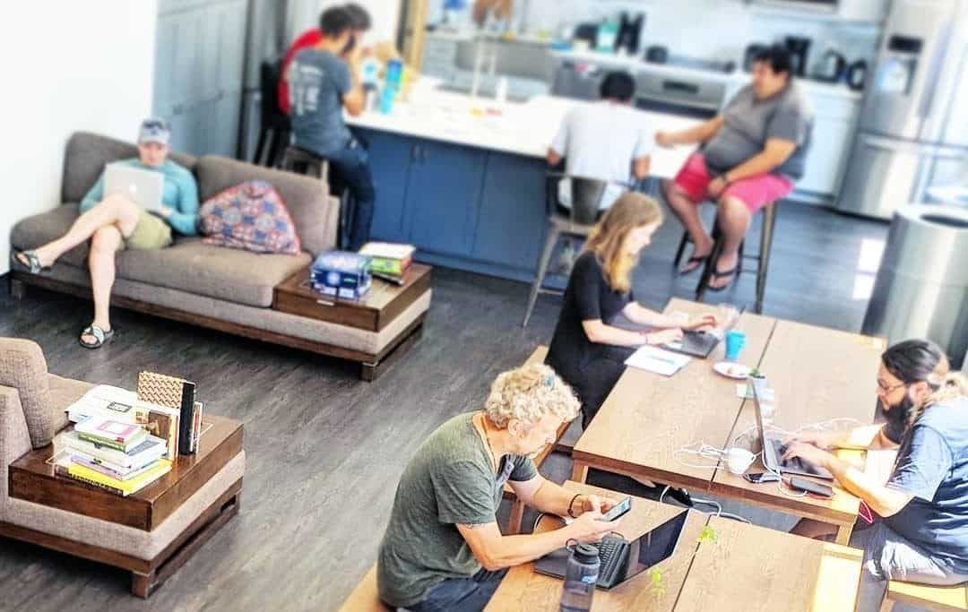 People in a co-working space: some on couches, some at tables working, others at the counter.