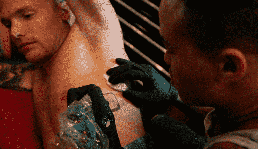 Man getting a tattoo on his chest in a studio; artist applying ink.
