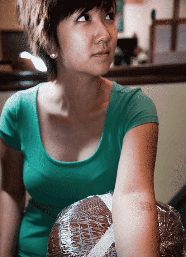 Woman in green shirt holding a packaged turkey, looking off to the side.