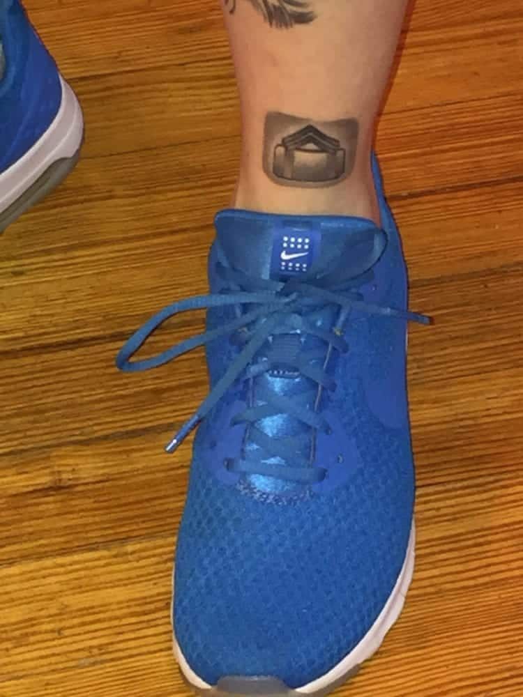 Blue sneaker with an ankle tattoo of an open envelope on a wooden floor.
