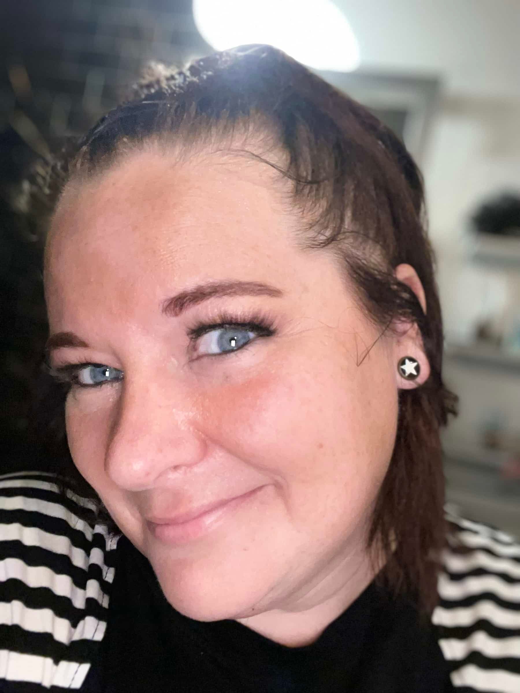 Woman with blue eyes, wearing a black and white striped shirt, smiling, with a star earring.