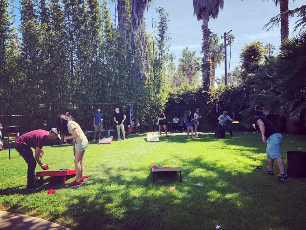 People playing cornhole on a grassy lawn, sunny day.
