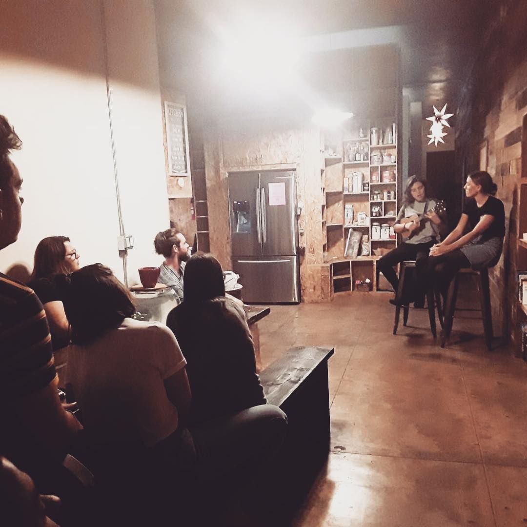 People listening to two women speaking at a small event in a rustic room.