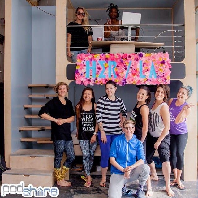Group of women at a yoga studio with a DJ, pink floral sign, and wood interior.