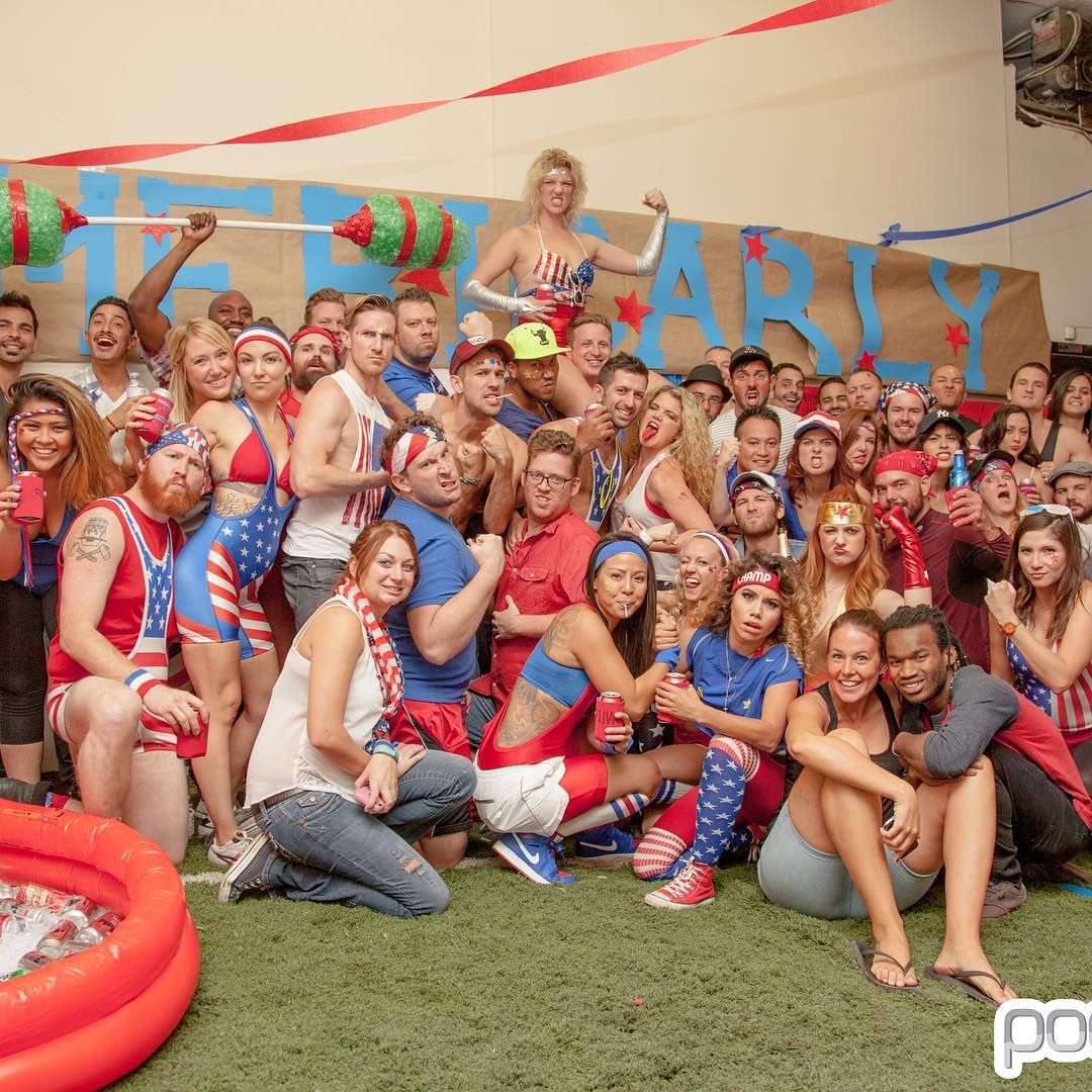 Group of people at a Fourth of July party, many in red, white, and blue, posing in front of a banner.