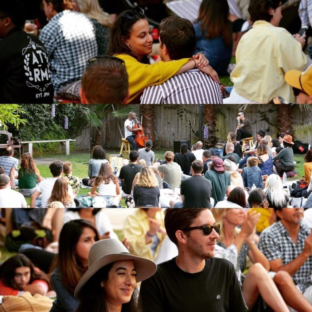 People at an outdoor concert, including a couple hugging and audience members seated on the grass.