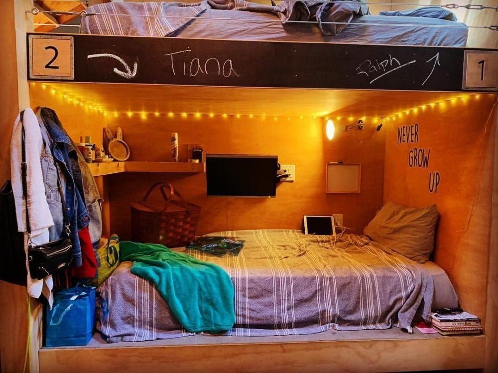 A cozy, wooden bunk bed setup with a TV, fairy lights, and personal items.