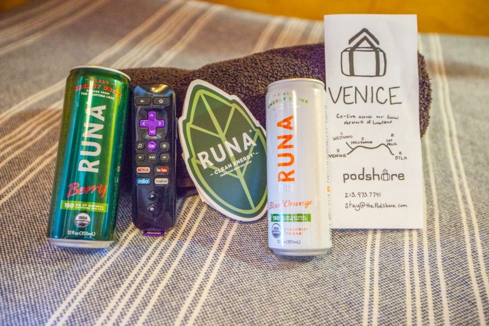 Two Runa cans, a Roku remote, leaf sticker, and Venice information on a striped blanket.