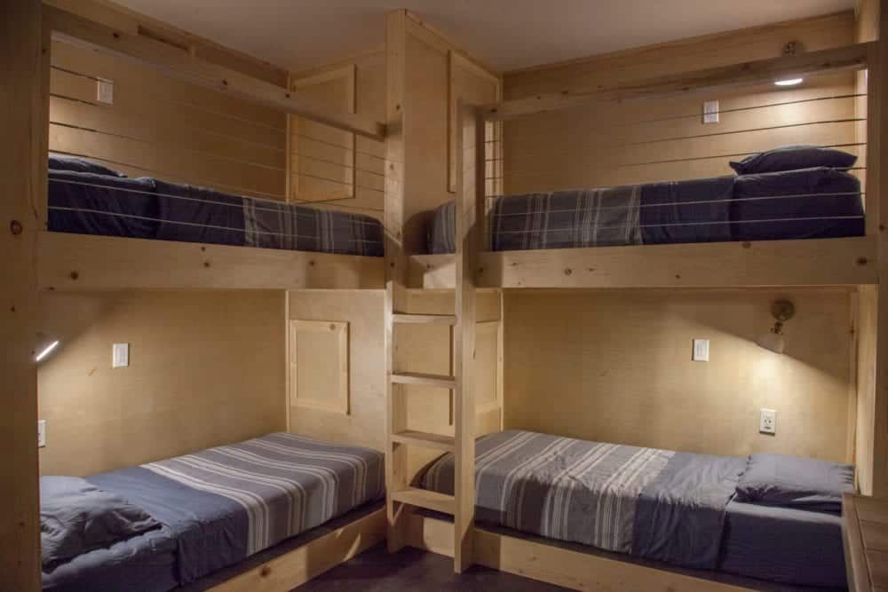 Four-person bunk bed room with wooden frames, two beds stacked, two ground-level beds; all with striped bedding.