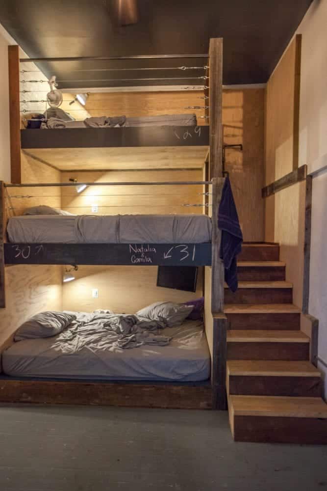 Bunk beds with gray bedding in a small room. Wooden stairs lead up to the top bunk.