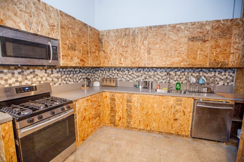 A kitchen with walls and cabinets made of oriented strand board, with appliances like a stove and microwave.