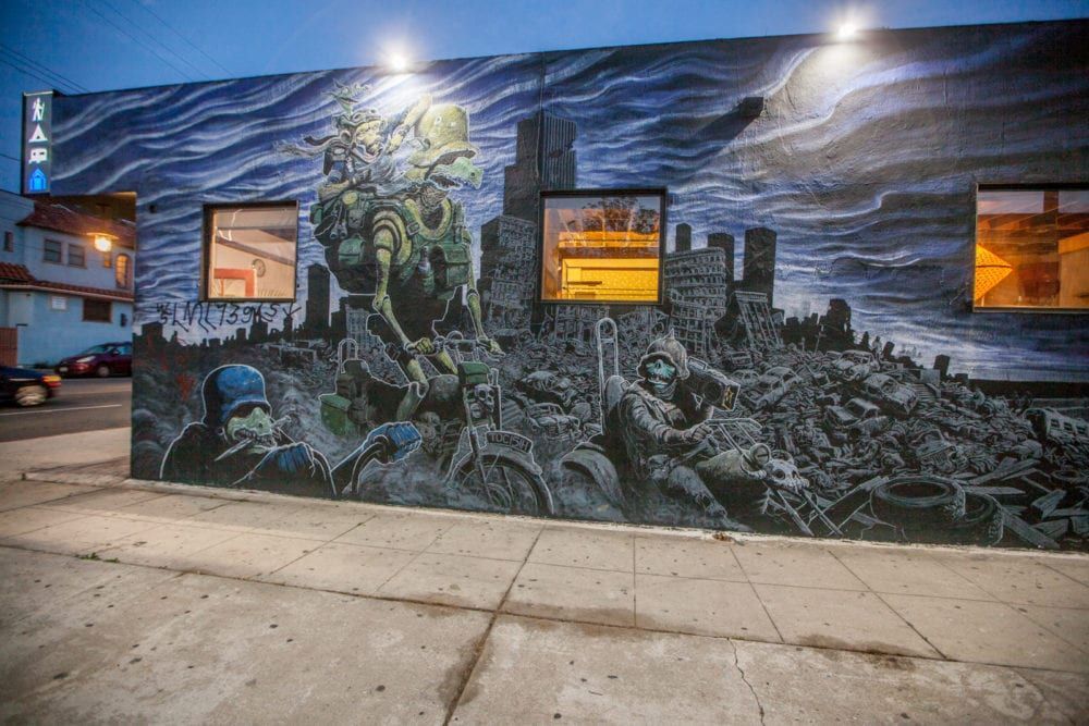 Mural of a post-apocalyptic scene with a large creature and cityscape, against a blue sky.
