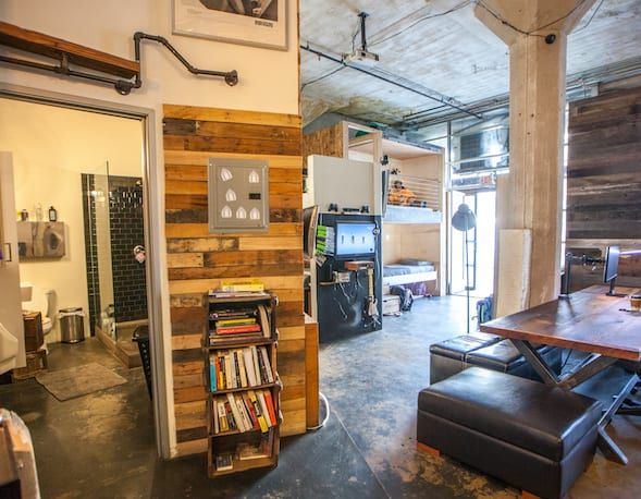 Interior with wooden wall, exposed pipes, and a view of a bathroom and living area.