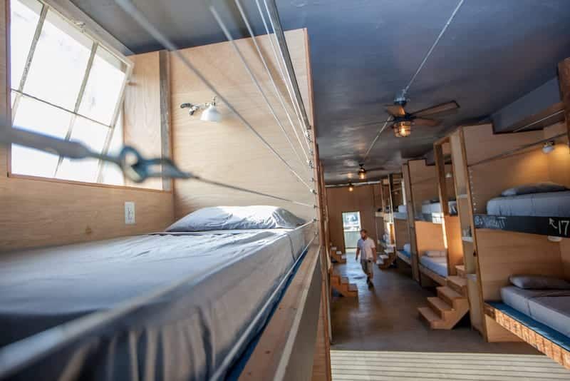 Bunk beds in a hostel room. A person walks in the aisle. Wooden structures and blue walls.
