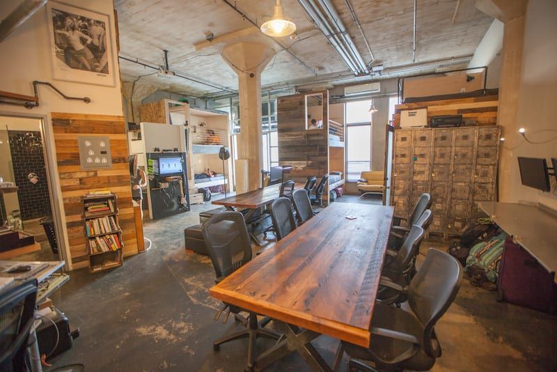 An open-plan office with a large wooden table surrounded by black office chairs.