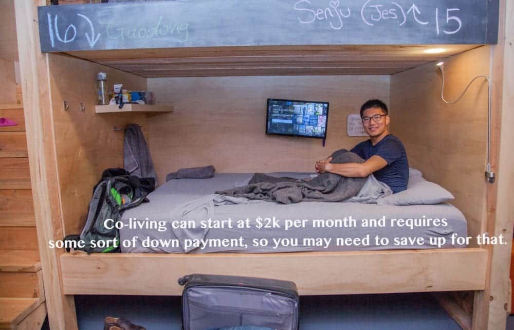 Man sits on a bed in a small co-living space. Text: Co-living starts at $2k with a down payment.