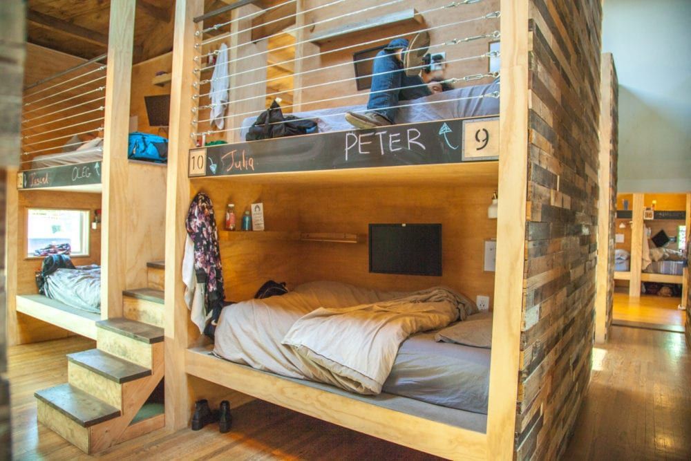 Bunk bed-style rooms. Wooden structures with sleeping spaces, stairs, and a person sitting on an upper bunk.