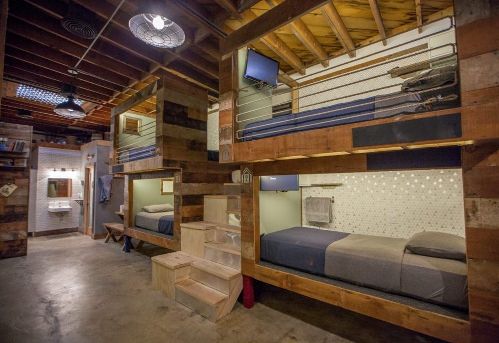 Indoor hostel with wood bunk beds and TVs. Concrete floors and exposed ceiling.