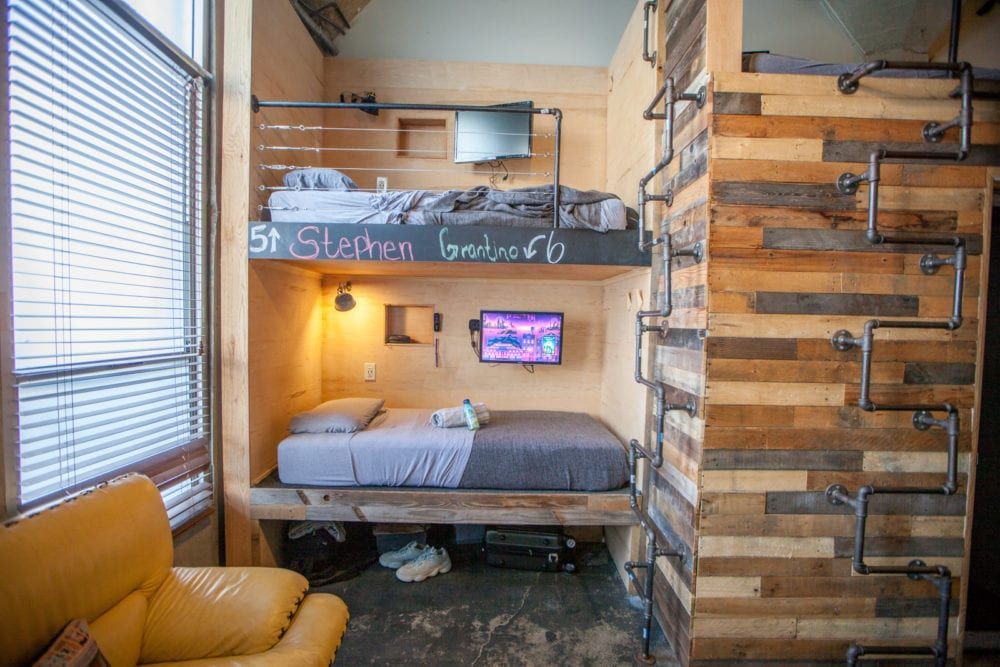 Small bunk bed alcove in a room with rustic wood paneling and industrial pipe ladders.