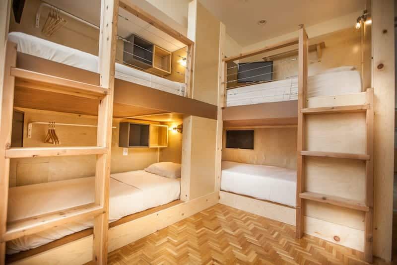 Bunk beds in a room, wood frames, white bedding, individual TVs. Wooden floor, light brown walls.