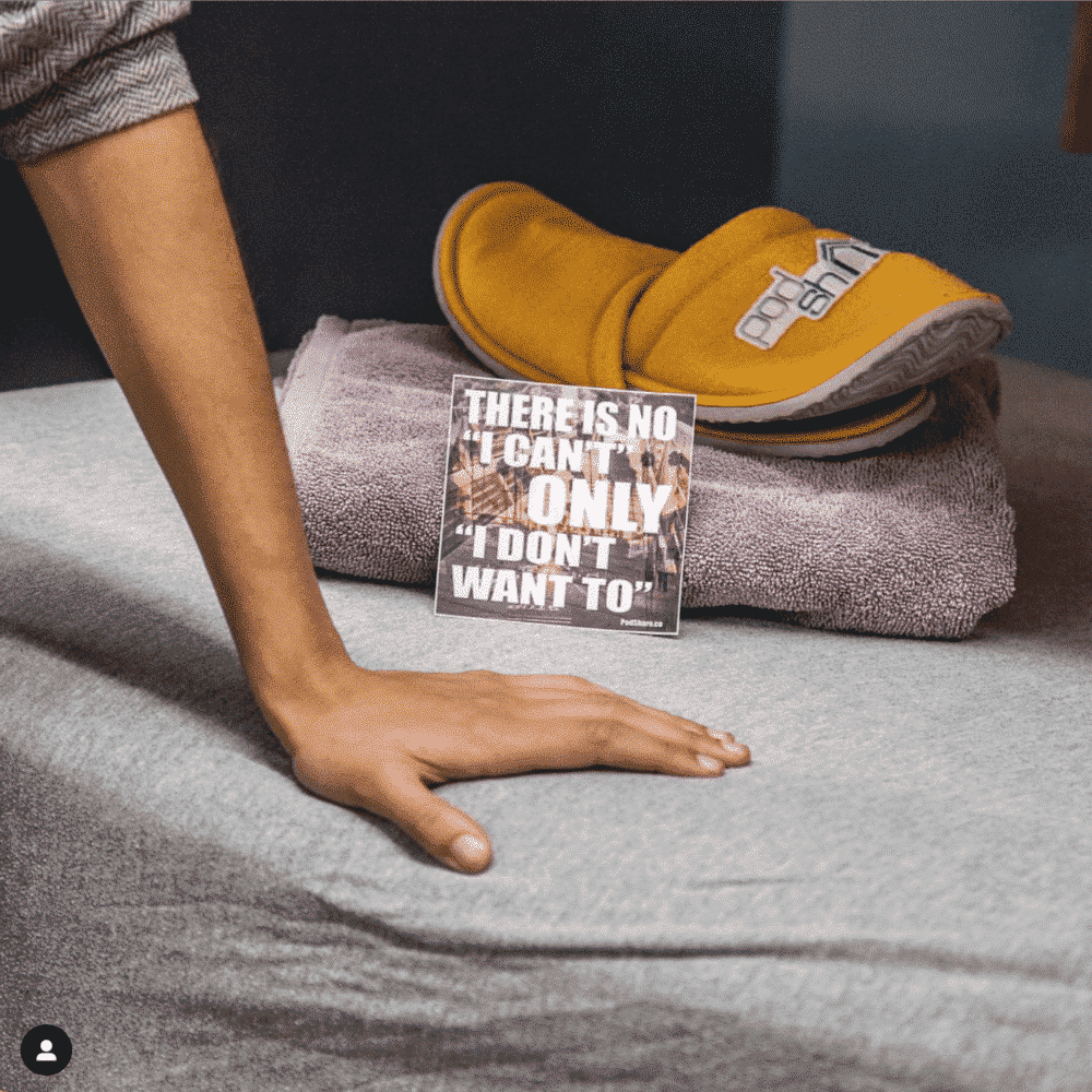 A person's arm resting on a grey surface; a pair of yellow slippers, a towel, and a motivational card.