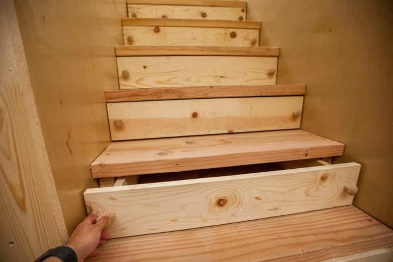 Wooden stairs being built inside a light-colored wooden enclosure. Hand holds a step in place.