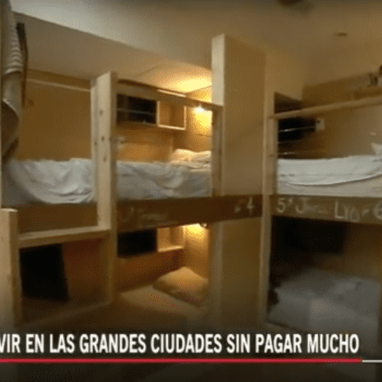 Bunk beds in a small room, suggesting affordable housing in a city. Wooden frames, white bedding, overhead lights.