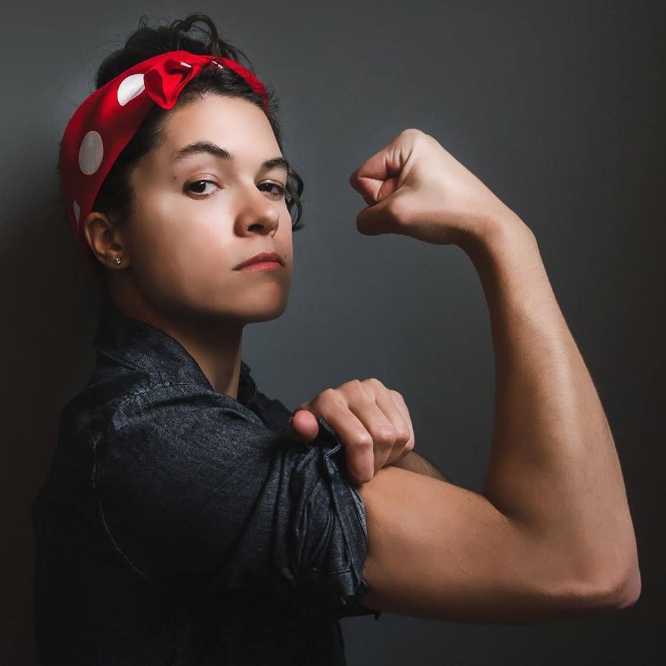 Woman in denim and red polka-dot headband flexes arm, emulating Rosie the Riveter.