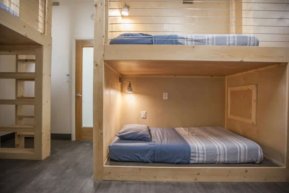 Bunk beds in a room, bottom bed enclosed with a window, lit by a small lamp.