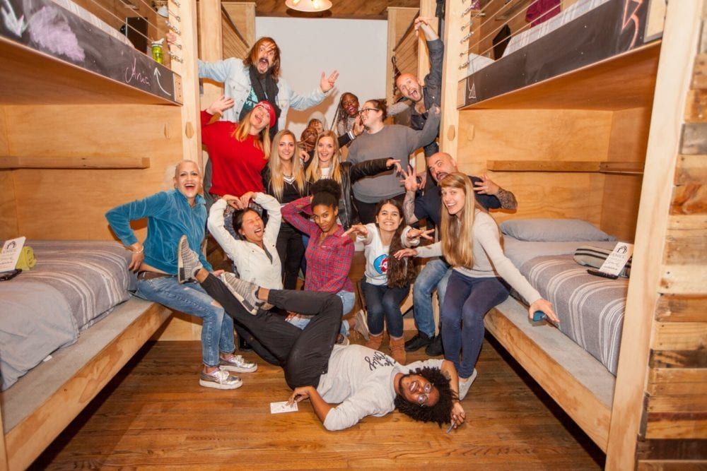 Group of diverse people joyfully pose in a wooden bunk bed room.