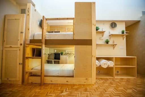 Wooden bunk beds in a small room with built-in storage and shelves. Light wood and white bedding.