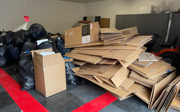 Garage interior with black trash bags and a pile of flattened cardboard boxes.