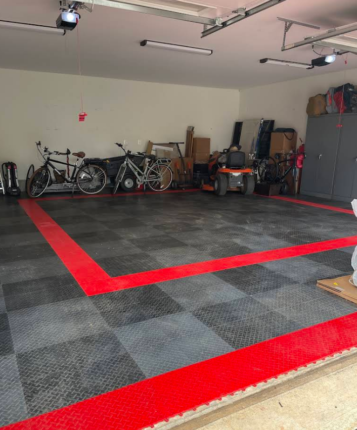 Garage with checkered floor, red border, bikes, mower, and storage cabinets.