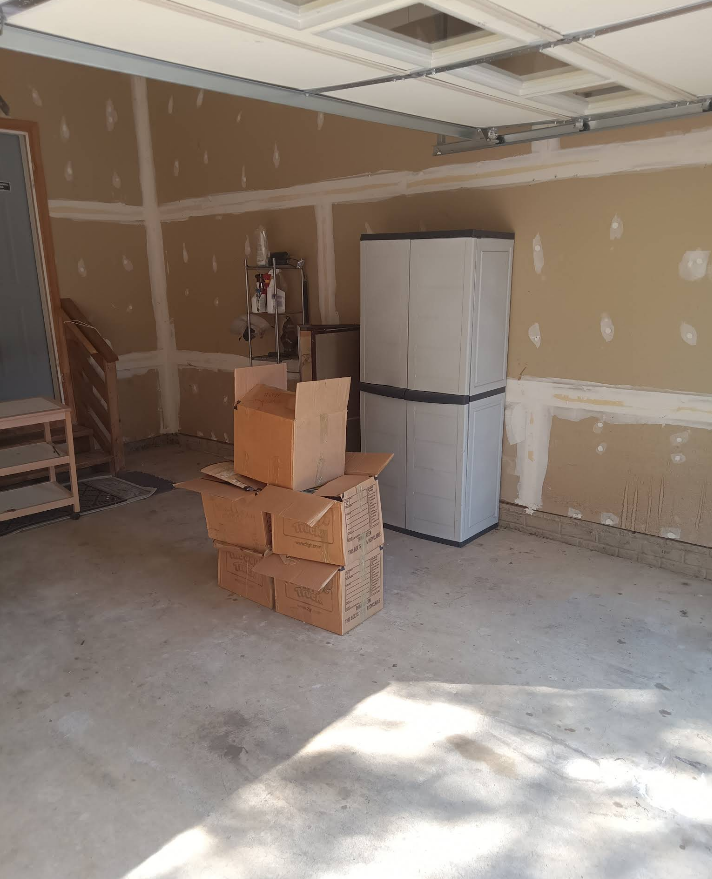 Garage interior with cardboard boxes, storage cabinet, and unfinished walls.