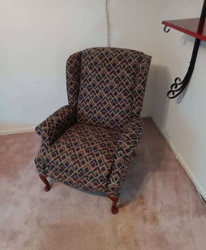Wingback armchair in a patterned fabric, sitting in a corner of a room on carpet.