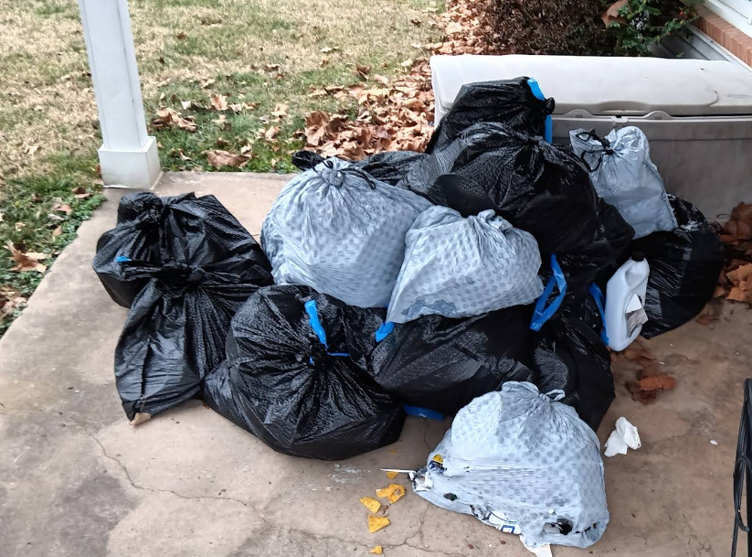 Pile of black and light blue garbage bags on a concrete porch, awaiting pickup.