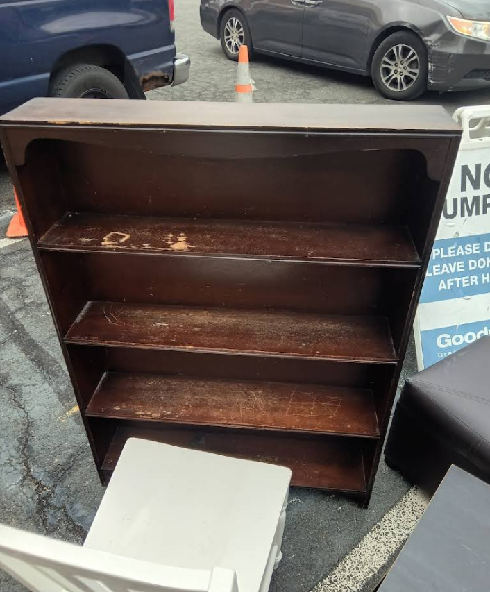 Dark brown bookshelf with three shelves; sitting outside on pavement.