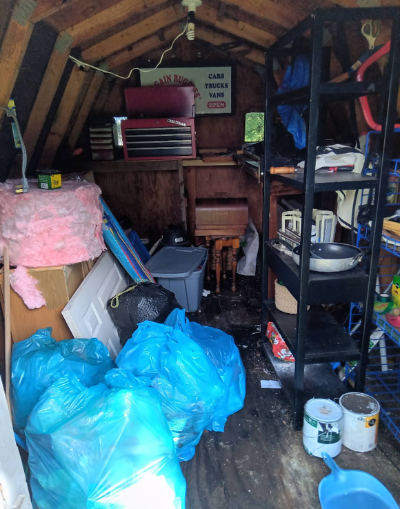 Interior of a cluttered shed with blue trash bags and storage shelves filled with items.