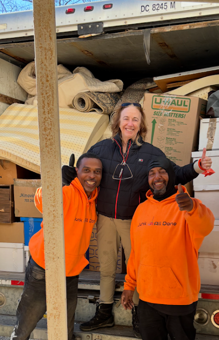 Three people smiling with thumbs up in front of a U-Haul truck loaded with boxes and furniture.