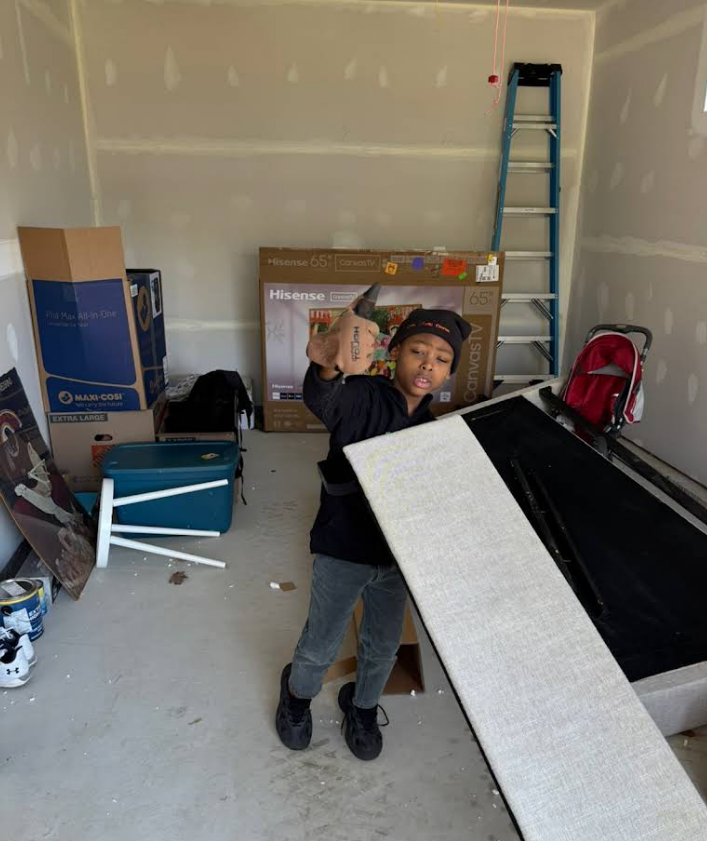Person holding a hammer, about to strike a white panel, in a garage with boxes and a ladder.