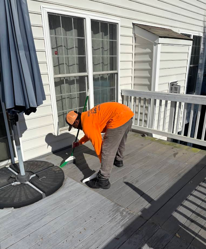 Person in orange shirt sweeping a wooden deck near a sliding glass door.