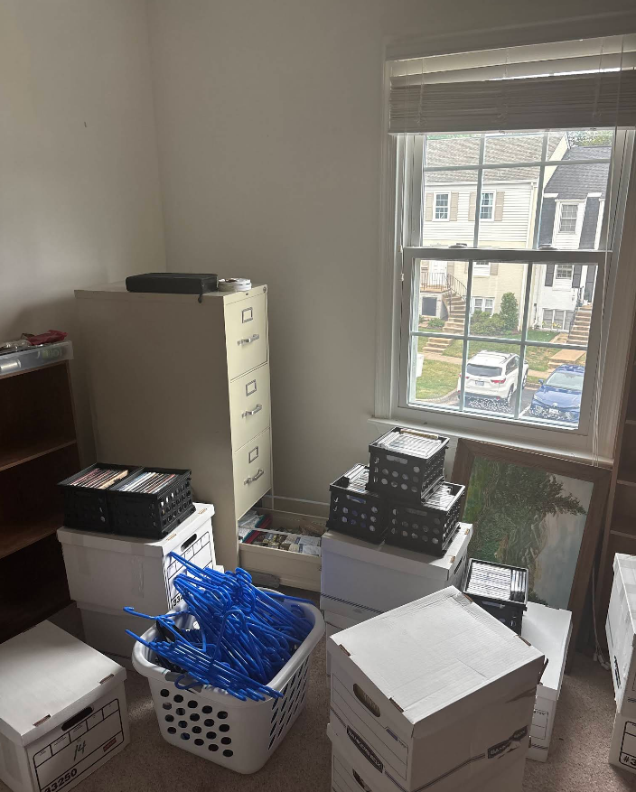 Room with boxes, a filing cabinet, a window, and miscellaneous items; appears to be in the process of being organized.