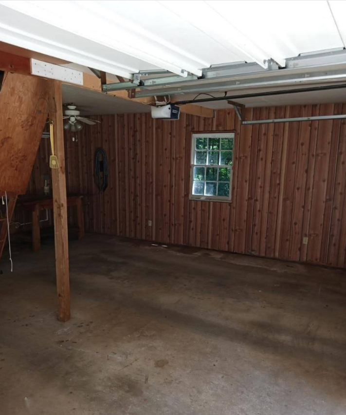 Empty garage with wood paneling, window, and garage door opener.