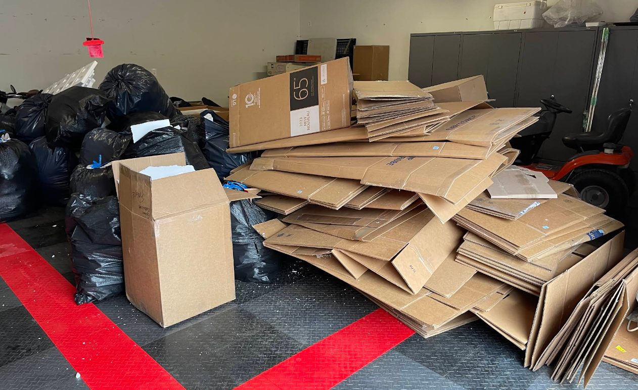 Piles of cardboard boxes and black trash bags inside a garage with a red line on the floor.