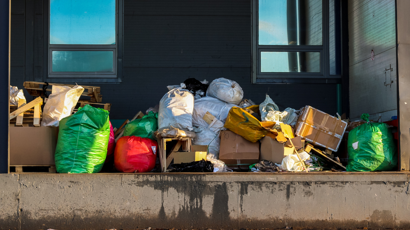 A pile of garbage bags and cardboard boxes in front of a building with blue windows.