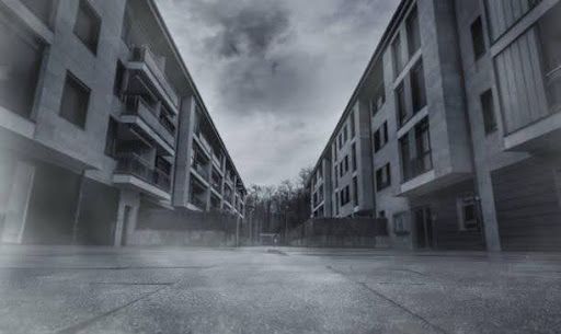 A low-angle view of two modern, grey apartment blocks separated by a central courtyard under a moody, overcast sky.