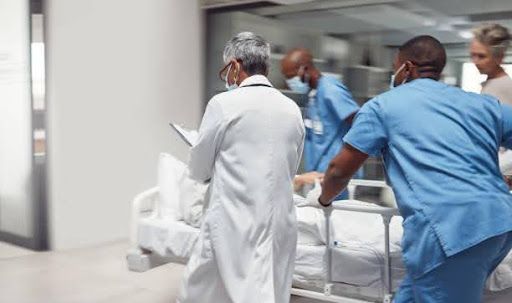 A team of medical professionals in scrubs and lab coats moves a patient on a gurney through a hospital corridor.