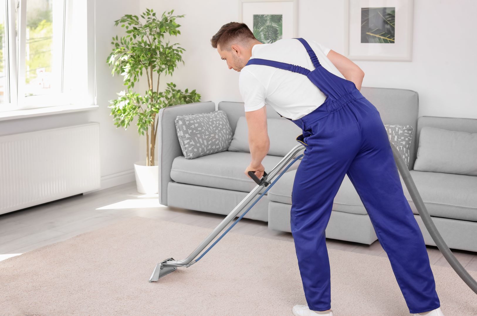 A man is using a vacuum cleaner to clean a carpet in a living room.