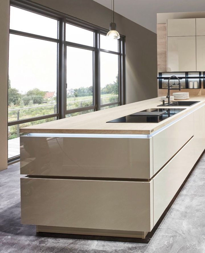 Modern kitchen with a large island, glossy tan cabinets, light countertops, and a window overlooking a field.